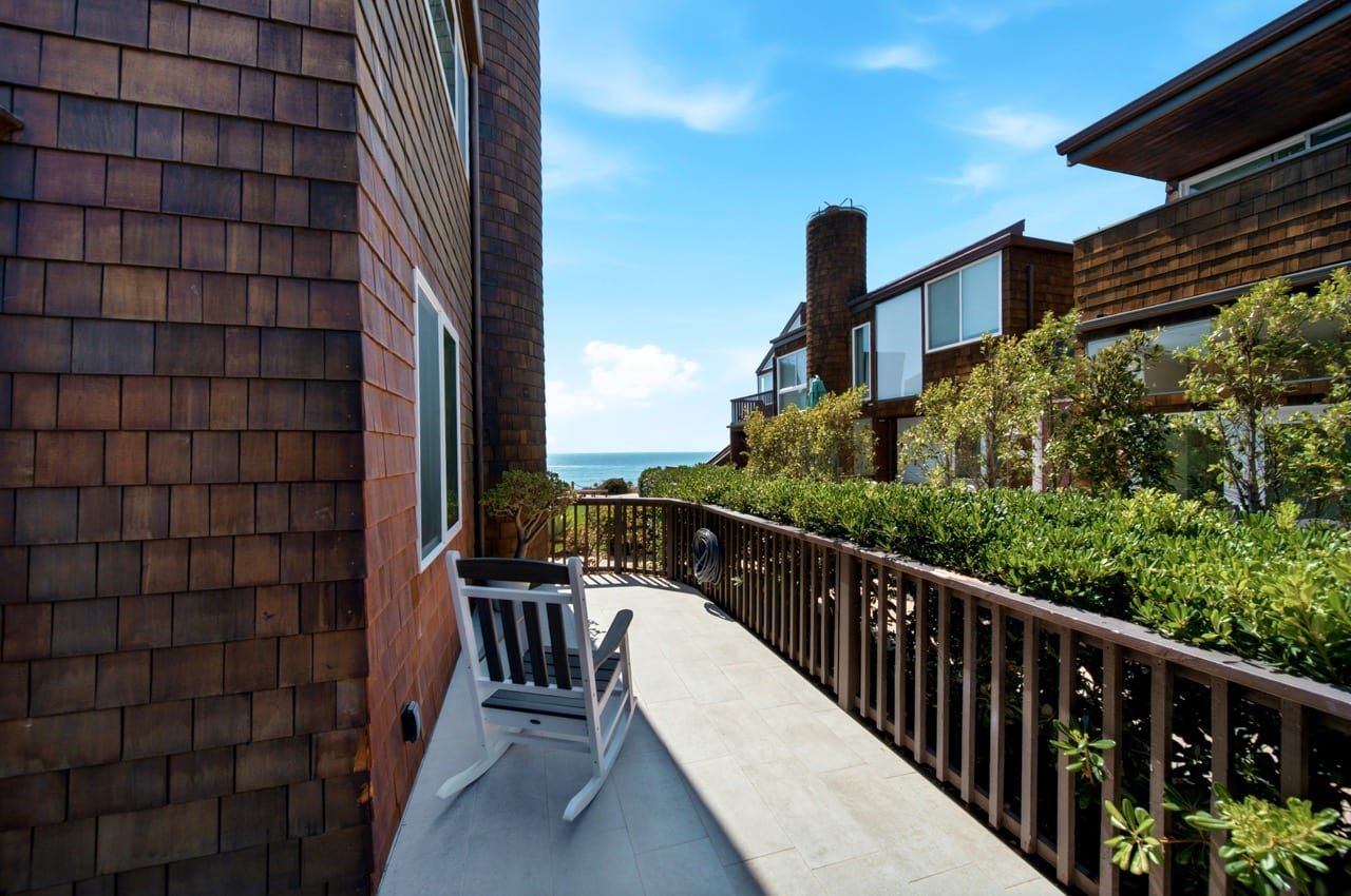 A rocking chair on the deck, the ocean visible past the hedge