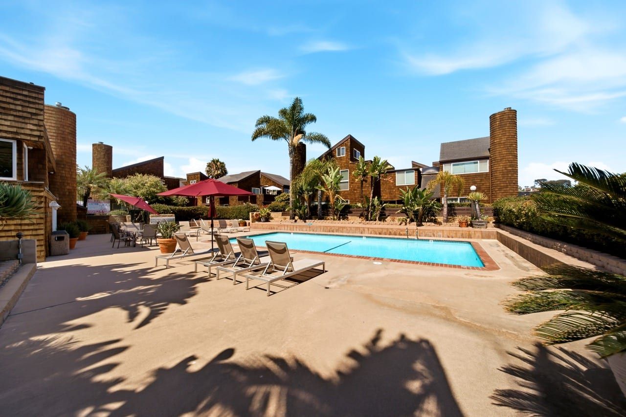 Loungers and shaded tables on the pool deck, palms and the shingled buildings beyond