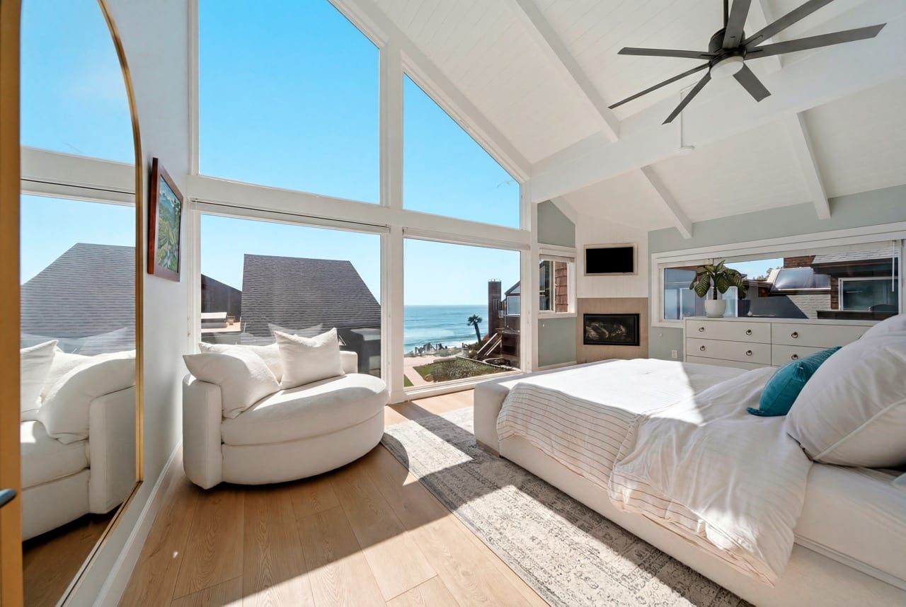 The primary bedroom by day, a wall of glass framing the ocean beside the bed