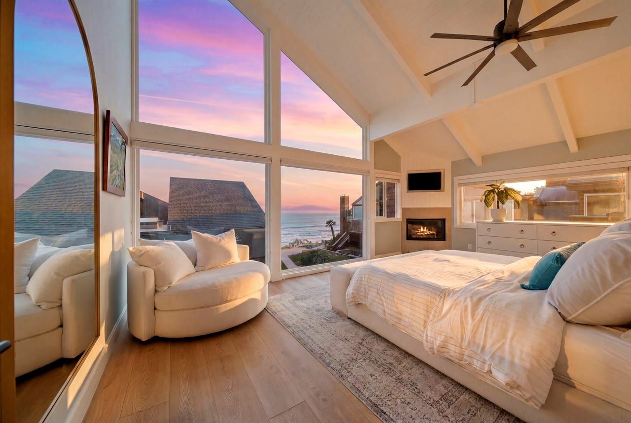 The primary bedroom at dusk, its gable window filled with a sunset over the Pacific